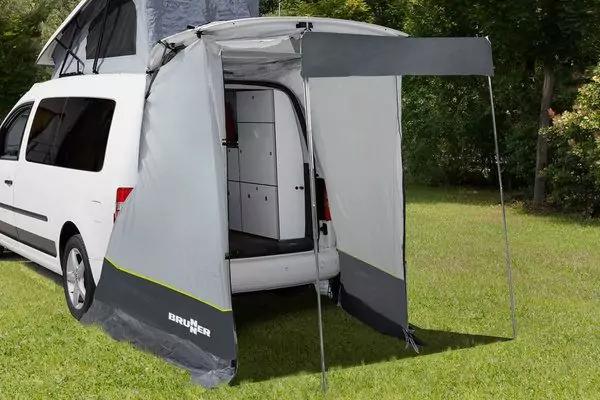 Wei&szlig;er Kleinbus mit aufgeklapptem Hochdach; am ge&ouml;ffneten Heck h&auml;ngt eine graue Heckannexe mit zwei St&uuml;tzstangen; Innenraum mit Schrank sichtbar; gr&uuml;ner Rasen und B&auml;ume im Hintergrund