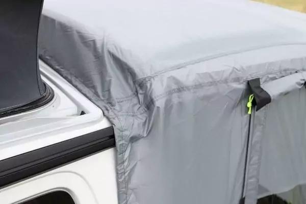 Nahaufnahme eines grauen Stoffbezugs mit N&auml;hten und Falten, befestigt an der Kante eines wei&szlig;en Fahrzeugs; schwarzer Gurt mit neon-gelber Zugschnur sichtbar