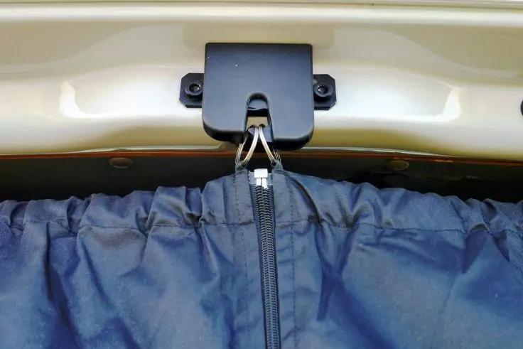 Beige lackierte Metallkante mit montierter schwarzer Hakenhalterung, an der ein Metallhaken einen dunkelblauen Stoffbeutel mit Rei&szlig;verschluss h&auml;lt