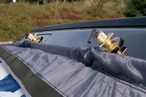 Zwei goldfarbene Spulen mit schwarzen Griffen an der Oberkante eines dunklen Dachs, im Vordergrund eine graue Plane, unscharfer Gras- und Baumbereich im Hintergrund