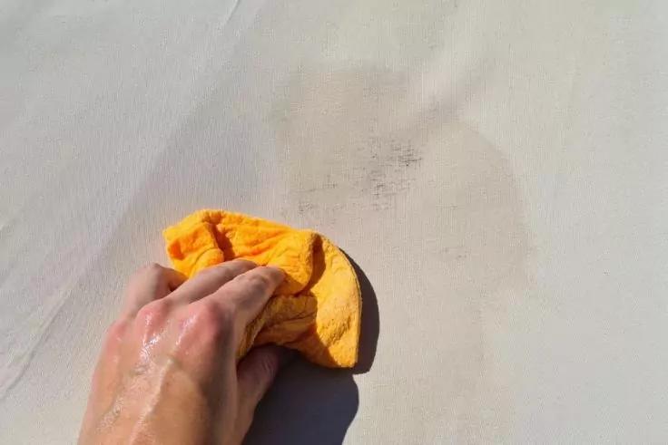 Fleck auf Zeltstoff wird mit Tuch beseitigt