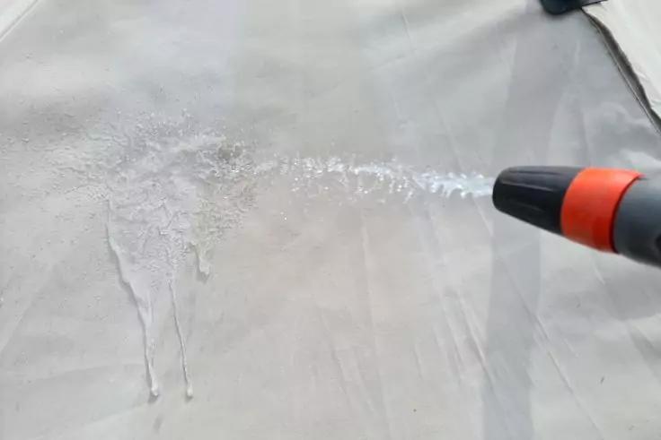 Zelthaut wird mit Wasserschlauch bespritzt.