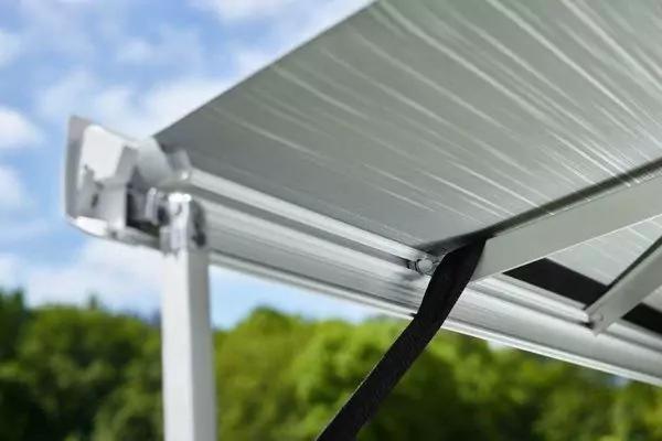 Metall&uuml;berdachung mit Aluminiumlamellen, schwarzem Gurt und wei&szlig;em St&uuml;tzpfosten; im Hintergrund B&auml;ume und blauer Himmel mit Wolken