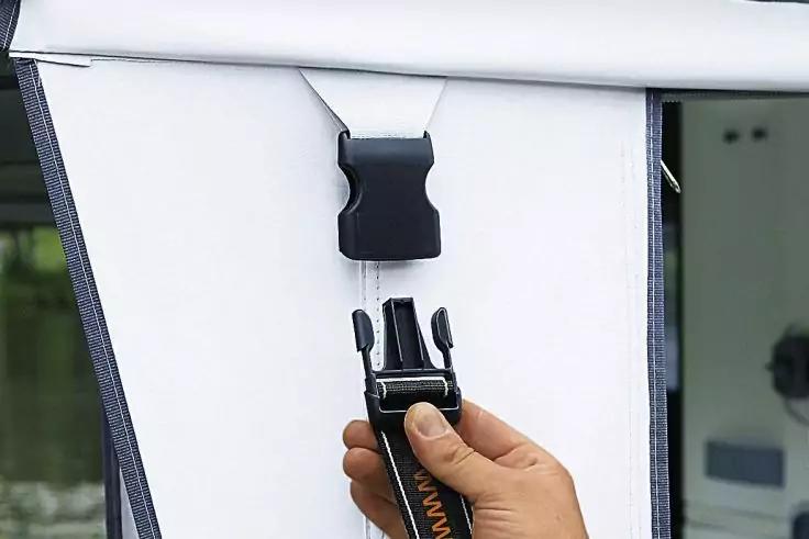 Nahaufnahme einer Hand, die einen schwarzen Kunststoffstecker an einen auf einer wei&szlig;en Stoffbahn mit schwarzem Rand befestigten schwarzen Gegenstecker h&auml;lt; im Hintergrund unscharfes Wasser