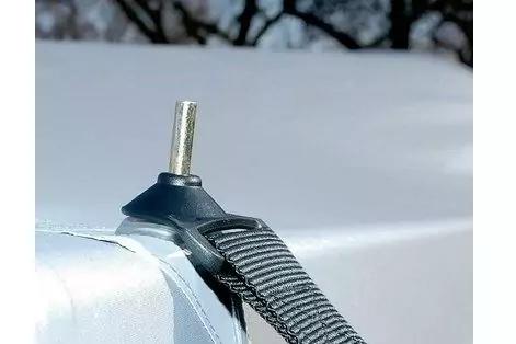 Schwarzer Gurt mit Kunststoffhalter und senkrechtem Metallstift auf wei&szlig;er Oberfl&auml;che, unscharfer verschneiter Hintergrund mit Baumsilhouetten