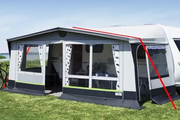 Wohnwagen mit angebautem wei&szlig;-grauem Vorzelt mit durchsichtigen Fenstern und gepunkteten Gardinen, ge&ouml;ffnete Eingangst&uuml;r, Tisch und St&uuml;hle innen, gr&uuml;ner Rasen, blauer Himmel, rote Markierungslinien auf dem Bild