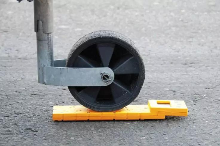 Schwarzes Rad mit Metallbefestigung auf orangefarbenem Kunststoffkeil auf Asphalt