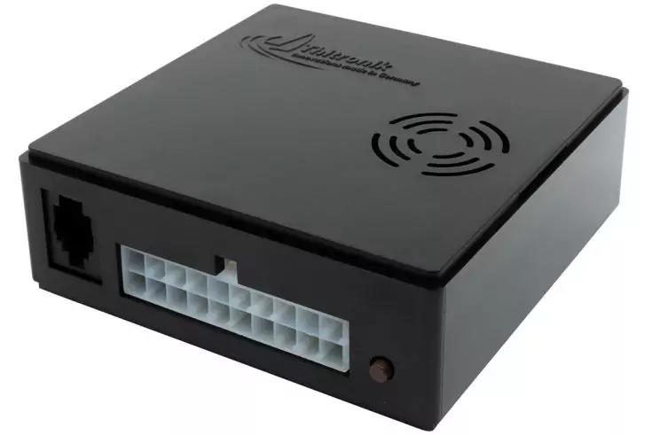 Schwarzes rechteckiges Kunststoffgehäuse auf weißem Hintergrund, vorn links ein RJ45-ähnlicher Anschluss, vorn mittig eine weiße mehrpolige Buchse, vorn rechts eine kleine runde Öffnung (LED), oben kreisförmige Lüftungsschlitze und ein aufgedrucktes