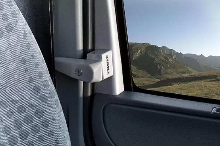 Hellgrauer, gemusterter Autositz, Gurtbefestigung an der B‑Säule, Türverkleidung und Fenster; durch das Fenster sichtbare Berglandschaft mit grünen Hängen und blauem Himmel