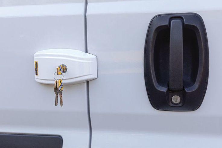 Weiße Lieferantür mit weißem Außen-Schlosskasten über der Türspalte, daran ein Schlüsselsatz; rechts schwarzer Türgriff