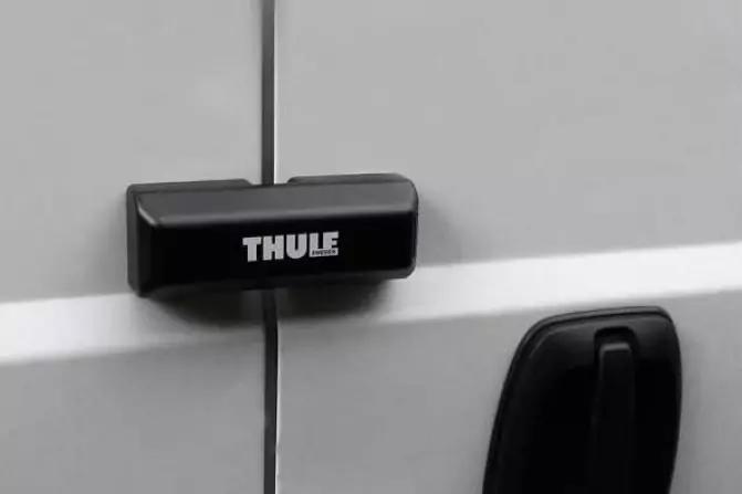 Schwarzes, rechteckiges Objekt mit Aufschrift "THULE" über der Türspalte eines weißen Fahrzeugs; schwarzer Türgriff rechts sichtbar