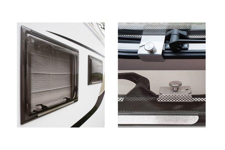 Links weiße Außenwand mit zwei rechteckigen Fenstern mit schwarzen Rahmen und geschlossenen Jalousien; rechts Nahaufnahme eines silbernen Metallverschlusses und eines Knaufs an einer schwarzen, strukturierten Kante