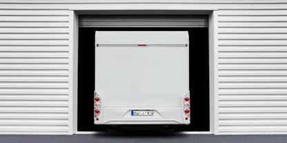 Heck eines wei&szlig;en Transporters, teilweise in einer offenen Garageneinfahrt; wei&szlig;e, geriffelte Au&szlig;enwand, dunkle Innen&ouml;ffnung, R&uuml;ckleuchten und Kennzeichen sichtbar