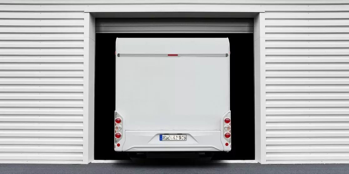 Heck eines wei&szlig;en Transporters, teilweise in einer offenen Garageneinfahrt; wei&szlig;e, geriffelte Au&szlig;enwand, dunkle Innen&ouml;ffnung, R&uuml;ckleuchten und Kennzeichen sichtbar