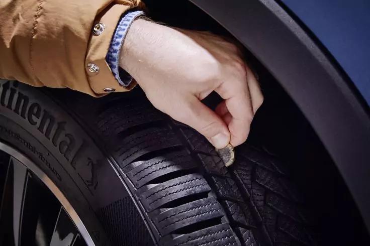 Hand h&auml;lt M&uuml;nze im Reifenprofil; Reifenflanke mit Schrift 'Continental', Felgenrand, &Auml;rmel und Uhr sichtbar