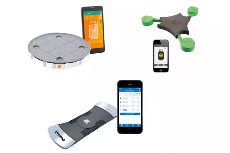 Runde Metallplatte oben links, daneben Smartphone mit orangefarbenem Bildschirm; oben rechts dreifl&uuml;geliges Ger&auml;t mit gr&uuml;nen Propellerabdeckungen und daneben Smartphone; unten links gebogenes wei&szlig;es Handger&auml;t; unten Mitte Smartphone mit blau-wei&szlig;em D