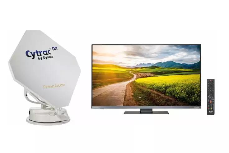 Weiße sechseckige Satellitenschüssel auf rundem Sockel mit Schriftzug 'Cytrac DX by Oyster'; daneben Flachbildfernseher, auf dem eine Landstraße zwischen Feldern, Hügeln und Himmel angezeigt ist; rechts eine Fernbedienung