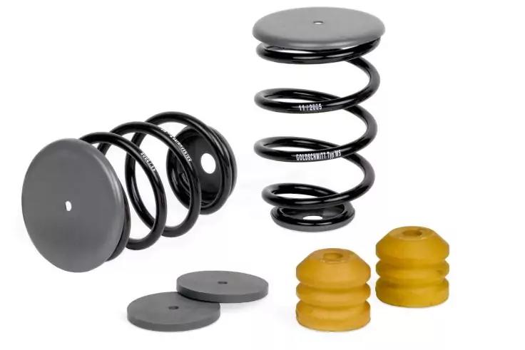 Zwei schwarze spiralf&ouml;rmige Federn, zwei schwarze runde Scheiben und zwei gelbe Gummipuffer auf wei&szlig;em Hintergrund