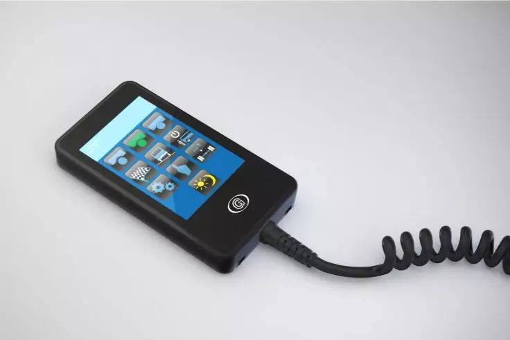 Schwarzes rechteckiges Ger&auml;t mit blauem Touchscreen und kleinen Symbolen, runder Knopf unter dem Bildschirm, spiralf&ouml;rmiges Kabel rechts angeschlossen auf hellgrauem Hintergrund