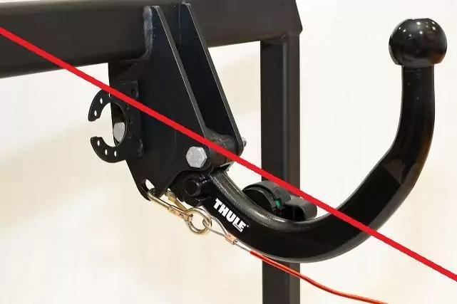 Schwarzes, gebogenes Metallteil mit Kugelkopf an einem schwarzen Rahmen; sichtbares "Thule"-Logo, rotes Kabel und diagonale rote Linie auf wei&szlig;em Hintergrund