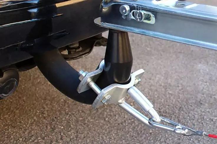 Metallkugel auf Halter mit zwei Schrauben, schwarzes Kabel in Schleife, Metall-Sicherheitskette mit Haken, Fahrzeugheckteil und Asphalt im Hintergrund