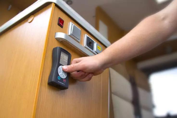 Hand h&auml;lt eine wei&szlig;e Karte vor einem schwarzen Kartenleser an einem Holzm&ouml;bel mit einer Reihe von Schaltern