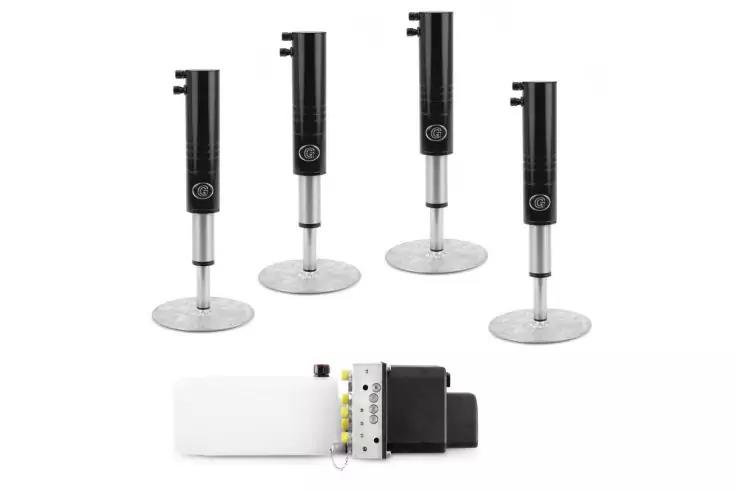 Vier schwarze zylindrische S&auml;ulen auf runden silbernen Platten nebeneinander; im Vordergrund ein wei&szlig;es rechteckiges Geh&auml;use mit einem schwarzen Anbauteil und sichtbaren elektrischen Anschl&uuml;ssen