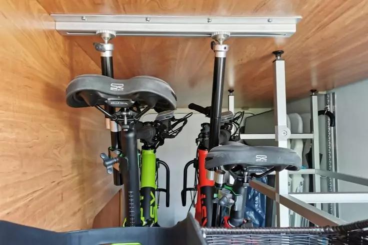 Zwei Fahrr&auml;der, eines mit gr&uuml;nem, eines mit rotem Rahmen, S&auml;ttel, Lenker und Vorderr&auml;der sichtbar; Metallschiene an Holzverkleidung; Metallregal rechts