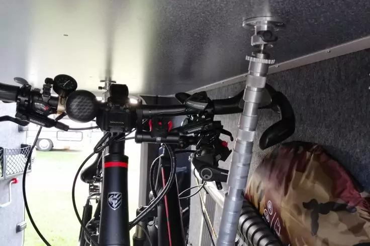 Teil zweier Fahrradrahmen mit Lenkern, Bremsz&uuml;gen und Vordergabeln, ein vertikales Metallrohr mit Klemme, eine tarnfarbene Tasche und graue Innenverkleidung