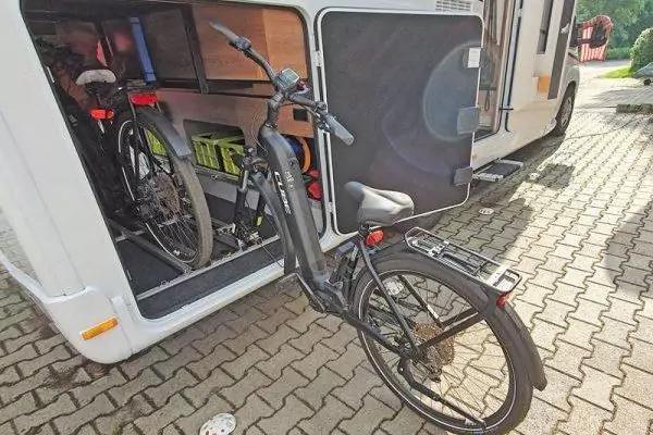 Zwei Fahrr&auml;der, eines teilweise aus einem offenen Gep&auml;ckfach eines wei&szlig;en Wohnmobils auf gepflastertem Boden