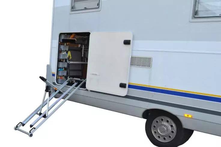 Seitenansicht eines Wohnmobils mit offenem Stauraumfach, sichtbaren Regalen und ausgeklappter Teleskopleiter zum Boden
