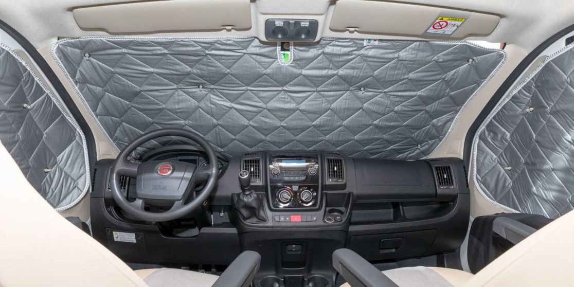 Innenansicht der Fahrerkabine eines Fahrzeugs, linksseitiges Lenkrad, silberne gesteppte Abdeckungen an Windschutzscheibe und Seitenscheiben, Armaturenbrett, R&uuml;ckspiegel, zwei Vordersitze