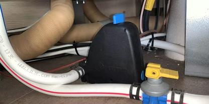 Innenraum unter einem Ger&auml;t: schwarzes Kunststoffgeh&auml;use mit blauem Verschluss, beige flexible Schl&auml;uche, wei&szlig;er Schlauch mit rotem Streifen, grauer Kunststoffanschluss mit gelbem Hebel und blauen Verbindungsst&uuml;cken, sichtbare Kabel