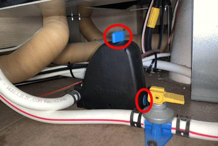 Unterseite eines Ger&auml;ts mit zwei braunen flexiblen Schl&auml;uchen oben, schwarzem Kunststoffhalter in der Mitte mit blauem Einsatz, wei&szlig;en und roten Schl&auml;uchen unten und blauem runden K&ouml;rper mit gelbem Hebel rechts