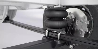 Nahaufnahme einer Fahrzeugaufh&auml;ngung mit zwei gestapelten schwarzen Gummib&auml;lgen, Metallhalterungen, U‑B&uuml;geln, Blattfeder und Achsrohr