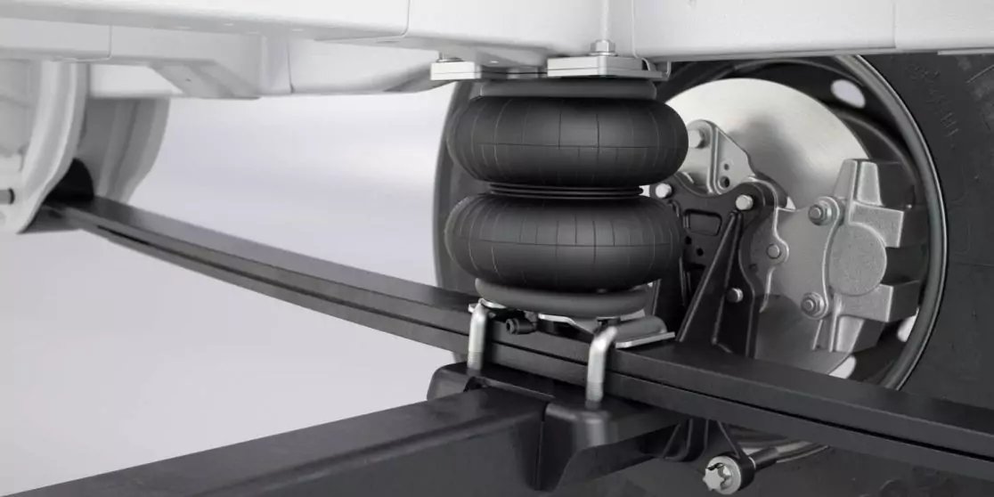 Nahaufnahme einer Fahrzeugaufh&auml;ngung mit zwei gestapelten schwarzen Gummib&auml;lgen, Metallhalterungen, U‑B&uuml;geln, Blattfeder und Achsrohr