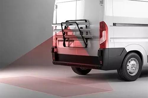 Heckansicht eines weißen Transporters mit montiertem Metallträger, schwarzen Gurten und roten, transparenten Dreiecken, die auf Boden und Fahrzeug projiziert sind