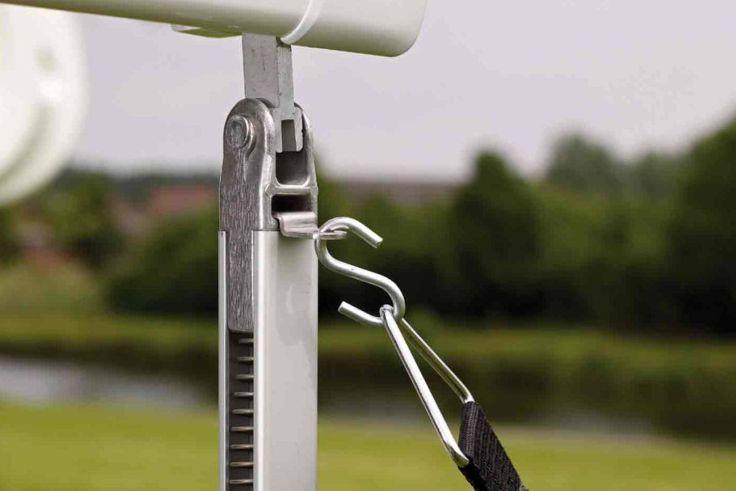 Nahaufnahme eines Metallhakens an einer senkrechten Metallstange, verbunden mit einem schwarzen Gurt, unscharfer Teich, Wiese und Bäume im Hintergrund