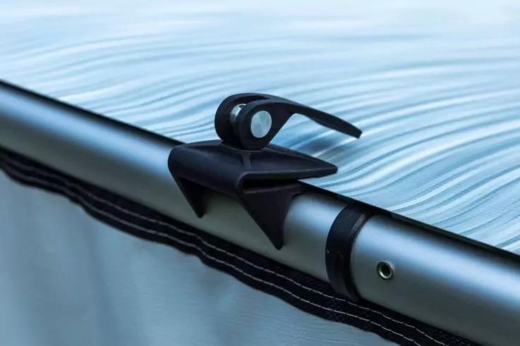 Schwarzer Kunststoffverschluss an einer silbernen Metallstange über hellblauem Stoff mit dunklem Saum