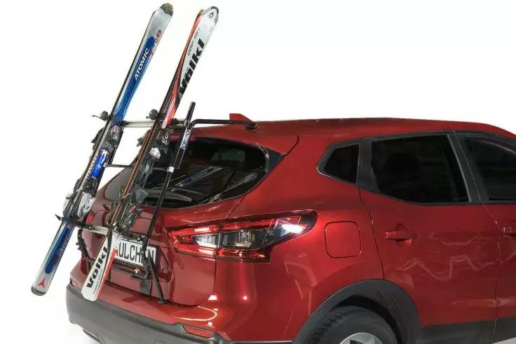 Rotes SUV von hinten rechts, an der Heckklappe montierter Skitr&auml;ger mit zwei Paar Skiern und Skist&ouml;cken, wei&szlig;er Hintergrund