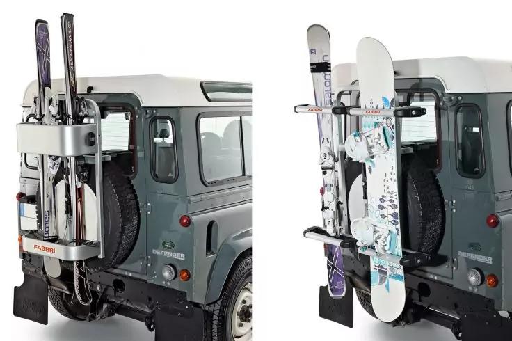 Heckansicht eines grauen Gel&auml;ndewagens mit montierter Halterung an der Heckklappe, die zwei Paar Ski und ein Snowboard h&auml;lt; Reserverad und R&uuml;cklichter sichtbar