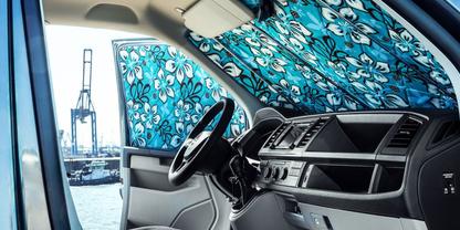 Innenraum eines Fahrzeugs mit Lenkrad und Armaturenbrett; Windschutzscheibe und Seitenscheibe mit blauem Blumen-Sonnenblendschutz; drau&szlig;en Hafenkran und Wasser sichtbar