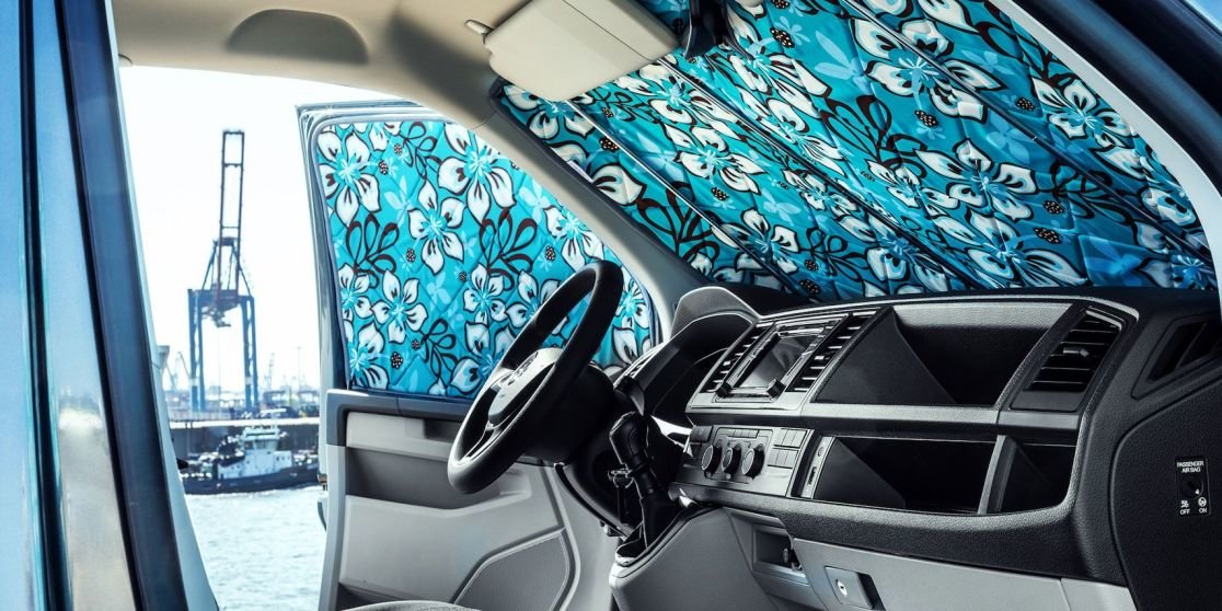 Innenraum eines Fahrzeugs mit Lenkrad und Armaturenbrett; Windschutzscheibe und Seitenscheibe mit blauem Blumen-Sonnenblendschutz; drau&szlig;en Hafenkran und Wasser sichtbar