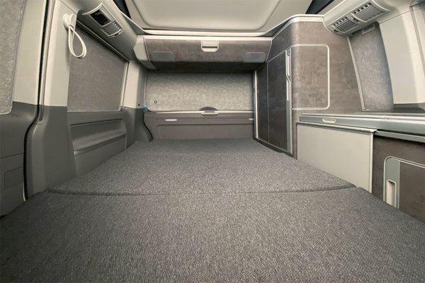 Innenraum mit flacher grauer Liegefl&auml;che, seitlichen Ablagen, einer vertikalen Schrankt&uuml;r und einer Deckenleuchte