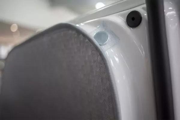 Nahaufnahme einer wei&szlig;en lackierten Metallkante mit grauem Stoffpolster, schwarzer Gummidichtung, runder schwarzer Plastikabdeckung und transparentem Kunststoffnietet