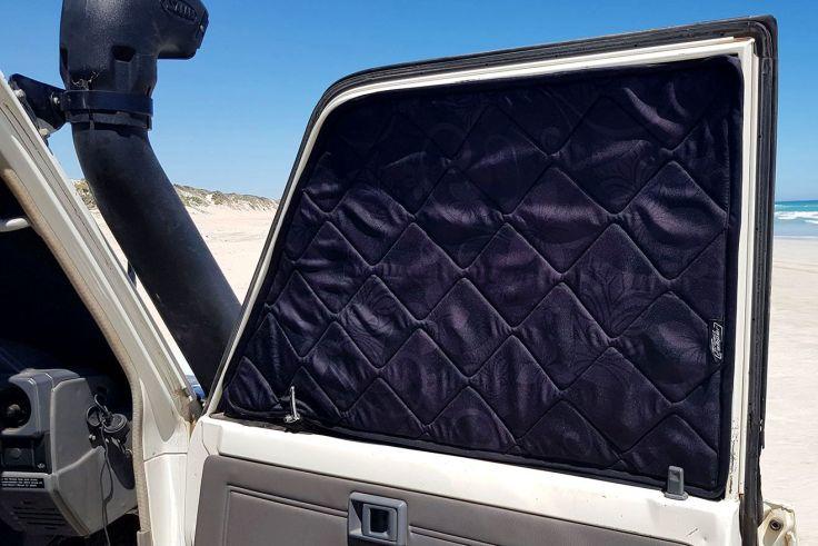 Offene Autot&uuml;r mit schwarzer, gesteppter Abdeckung an der Innenseite des Fensters; im Hintergrund Sandd&uuml;ne, Meer und blauer Himmel