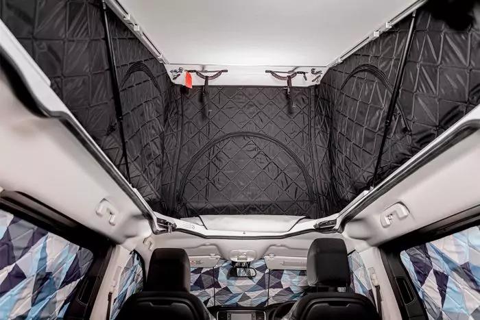 Fahrzeuginnenraum: hochgezogene schwarz gesteppte Stoffdecke, zwei Vordersitz-Kopfst&uuml;tzen, wei&szlig;e Deckenr&auml;nder, seitliche blau-graue geometrische Vorh&auml;nge