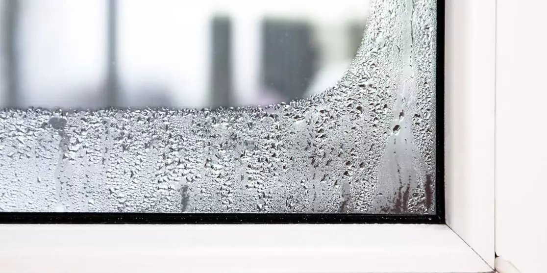 Wei&szlig;e Fensterecke mit Wassertropfen auf der Glasscheibe und unscharfer Au&szlig;enansicht