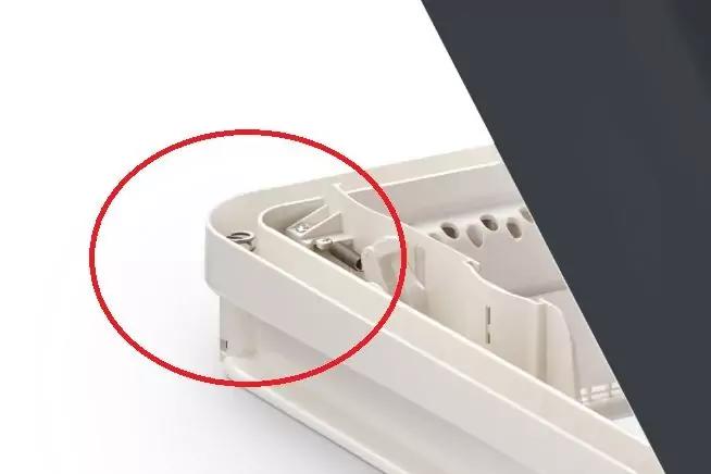 Nahaufnahme eines weißen Kunststoffrahmens mit Aussparungen und kleinem Metallclip in der Ecke, roter Kreis um die Ecke, weißer Hintergrund
