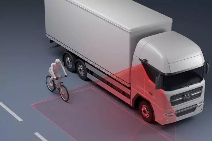 Wei&szlig;er Lkw auf Stra&szlig;e, rote projizierte Fl&auml;chen vorne und seitlich, eine Person auf einem Fahrrad neben dem Lkw